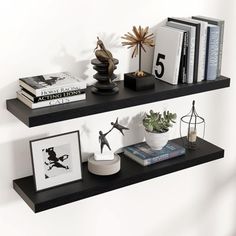 two black floating shelves with books, vases and other items on them in front of a white wall