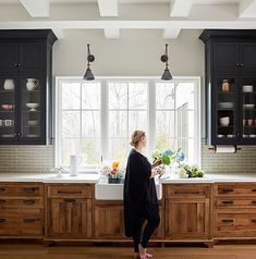 a woman standing in front of a kitchen sink with lots of counter space and cabinets