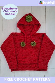 a red crocheted hoodie with green buttons on the front and bottom, sitting on top of a white wooden floor