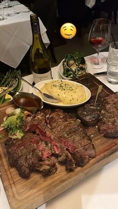 a wooden cutting board topped with steak and mashed potatoes next to bottles of wine