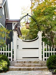 a white gate in front of a house with steps leading up to it and trees