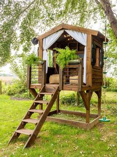 a tree house with a deck and stairs leading up to the upper level, surrounded by green grass