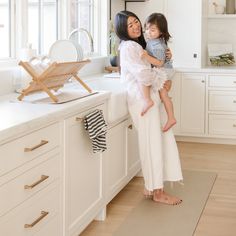 a woman holding a child in her arms while standing next to a kitchen counter top