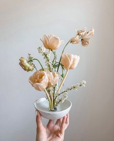 a person holding a white bowl with flowers in it and the bottom half of their hand