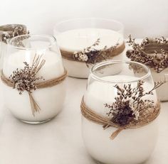 four glass vases with dried flowers and twine tied around the inside are sitting on a white surface