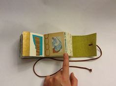 a hand is pointing at an open book on a white table with a string attached to it