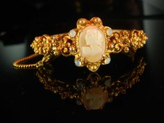 "This victorian style vintage bracelet holds a genuine cameo. Signed Florenza. Ornate raised baroque flowers surround the beautiful center piece genuine cameo on this stunning and charming hinged bangle bracelet. The stones are around it are faux moonstones which give it quite an eerie effect. The bracelet measures 7\" long on the inside and it has its original safety chain. The back of the band has ornate fancy etchings. The hinge and clasp work well. Inside it is marked Florenza. 2-2-19" Baroque Bracelet, Baroque Flowers, Claddagh Bracelet, Victorian Bracelet, Diamond Jewel, Safety Chain, Vintage Bracelet, Bracelet Vintage, Hinged Bangle