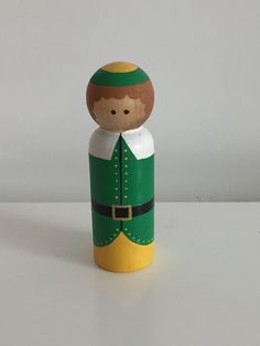 a wooden toy with a green and yellow outfit on it's head is sitting on a white surface