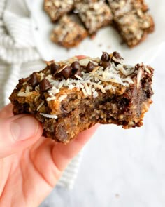 a person holding up a chocolate chip cookie with coconut flakes on it's side