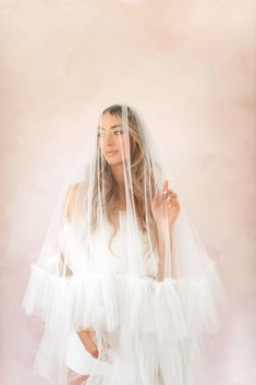 a woman wearing a veil and white dress posing for the camera with her hands on her hips