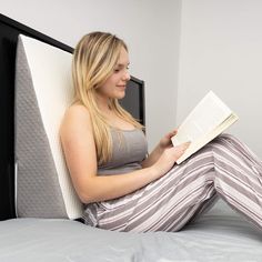 a woman sitting on a bed reading a book while wearing striped pants and tank top