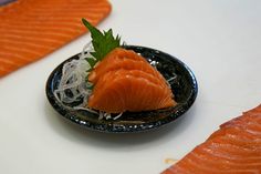 there is a small black plate with some salmon on it and another piece of fish in the background