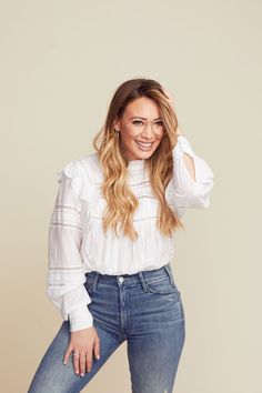 a woman posing for a photo with her hand on her head and wearing blue jeans