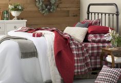 a bedroom decorated for christmas with red and white bedding, plaid blanket, green wreaths on the wall