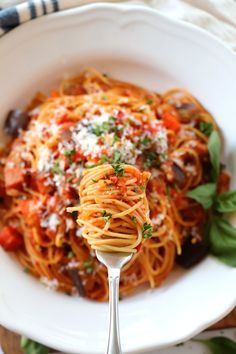 a white bowl filled with pasta and sauce on top of a wooden table next to a fork