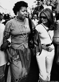 two women are walking down the street with other people behind them in black and white