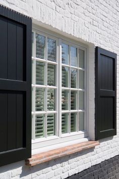 an open window with black shutters on a white brick building