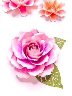 three paper flowers with green leaves on white background, one pink and one orange flower