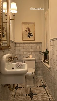 a white toilet sitting next to a sink in a bathroom under a painting on the wall