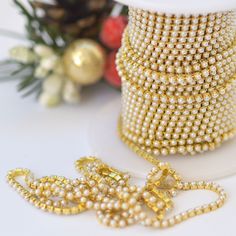 a spool of gold beaded ribbon next to a roll of beads on a white surface