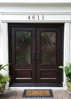 the front door to a home with two glass doors and potted plants on either side