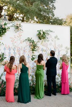 a group of people standing next to each other in front of a wall with flowers on it