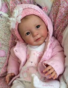 a baby doll that is laying down on a bed with pink clothes and bonnets