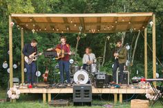 a group of people that are standing on a wooden platform in the grass with guitars