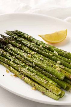 asparagus on a white plate with lemon wedges and seasoning next to it