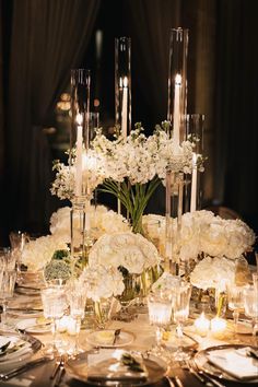 a table with candles and flowers in vases on top of it, surrounded by silverware