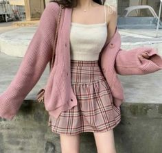 a woman wearing a pink cardigan sweater and plaid miniskirt is posing for the camera