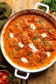 a pan filled with meatballs and sauce on top of a wooden table next to tomatoes