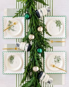 the table is set for christmas dinner with green and white plates, silverware and greenery