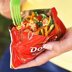 a person holding a bag of food with a fork in it's hand and a plastic fork sticking out of it