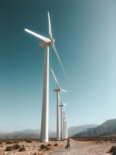 a person walking down a dirt road next to wind turbines