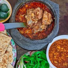 a table topped with plates and bowls filled with food next to pita breads