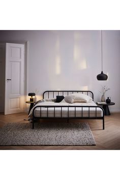 a bed sitting on top of a wooden floor next to a white wall and lamp