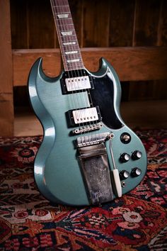 a blue electric guitar sitting on top of a carpeted floor next to a wooden wall