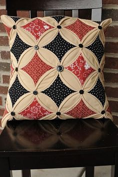 a black and red pillow sitting on top of a wooden chair next to a brick wall