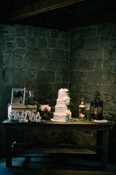 a wedding cake sitting on top of a wooden table next to a stone wall with candles