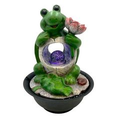 a frog statue sitting on top of a bowl filled with water and rocks, holding a flower