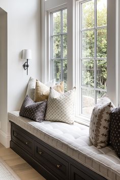 a window seat with pillows on it in front of two windows, one is white and the other is black