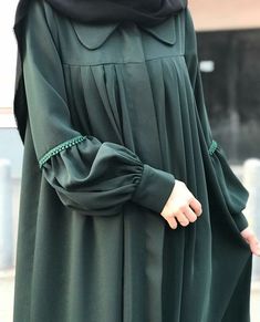 a woman in a green dress is holding her hand out to the side while wearing a black hijab