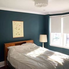 a bed sitting in a bedroom next to two windows with blinds on the window sill