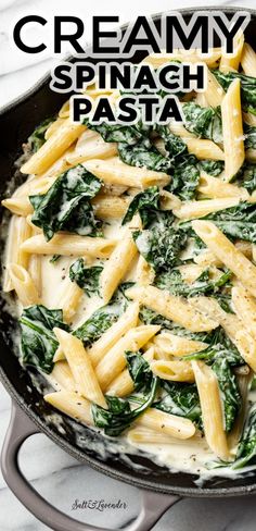 pasta with spinach and white sauce in a skillet on a marble countertop