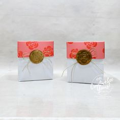 two small white boxes with red and pink designs, one has a gold coin in it