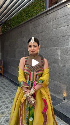 a woman in a yellow and brown dress standing next to a wall with her hands on her hips