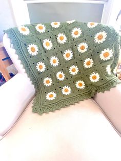 a green crocheted blanket with sunflowers on it sitting on a white chair