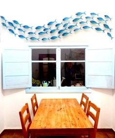 a wooden table and chairs in front of a window with blue fish on the wall