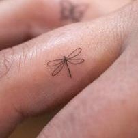 a small dragonfly tattoo on the left side of someone's right hand,